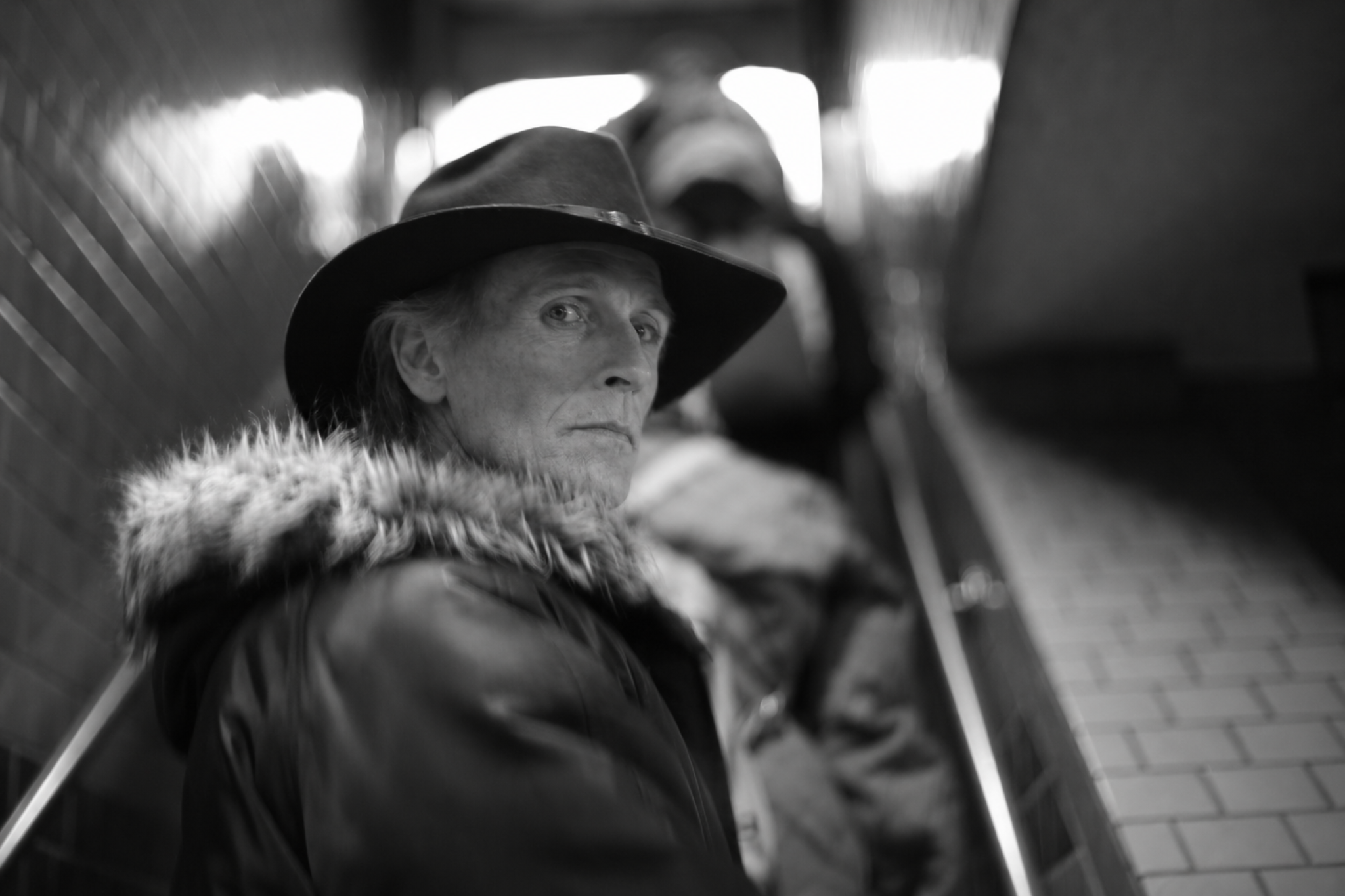 Silas Crowe turning on an escalator in a black hat and winter coat